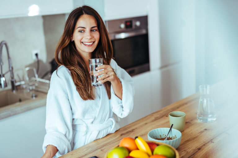 Frau trinkt Glas Wasser im Bademantel Küche
